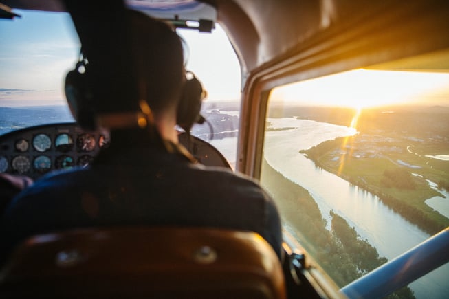 A Certified Flight Instructor sits in the right seat as a student flies next to a river during the golden hour