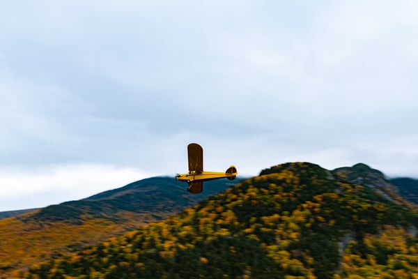 A Piper Cub flying over a rural landscape