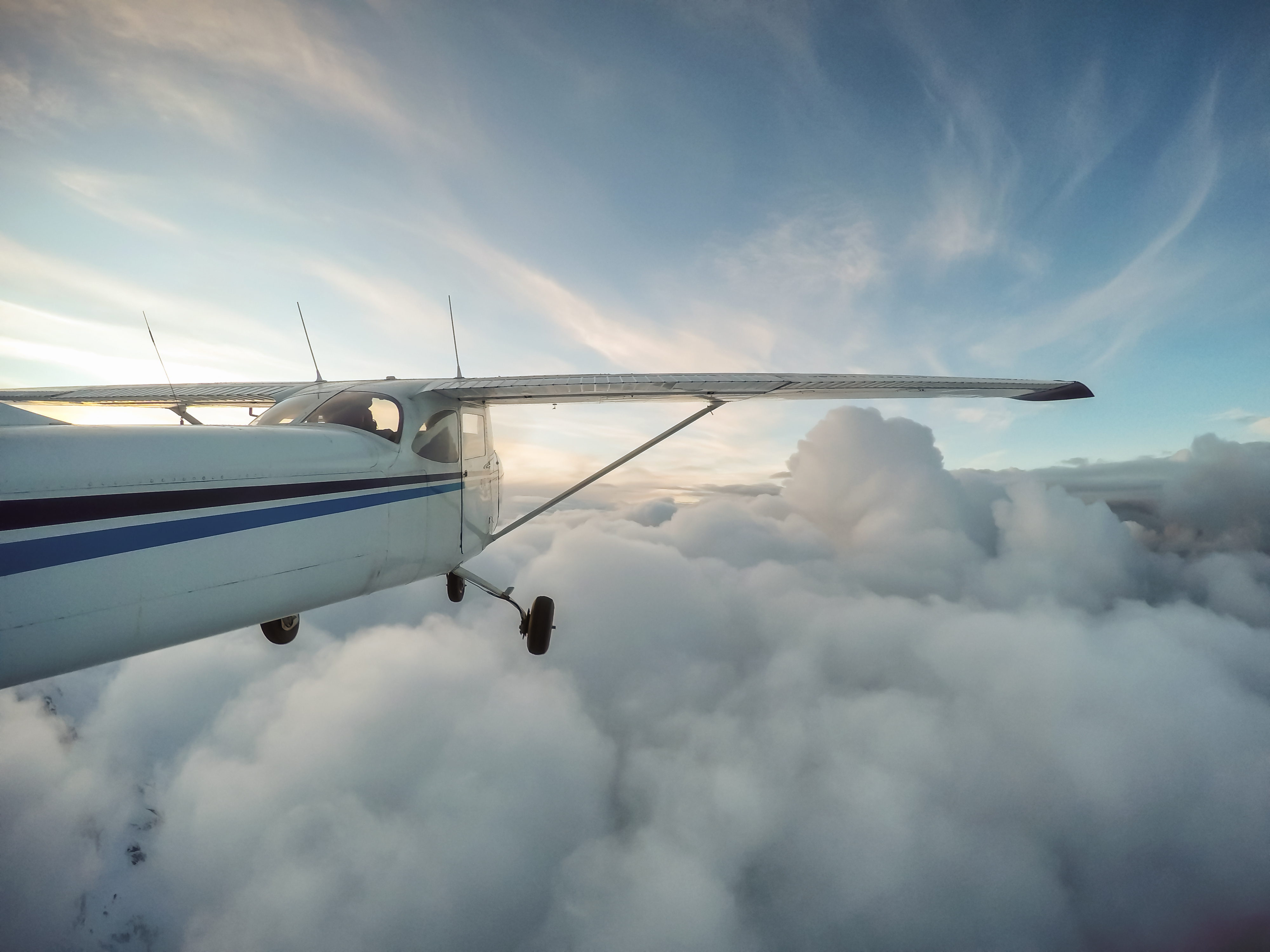 GA high-wing plane flying just over the top of the clouds