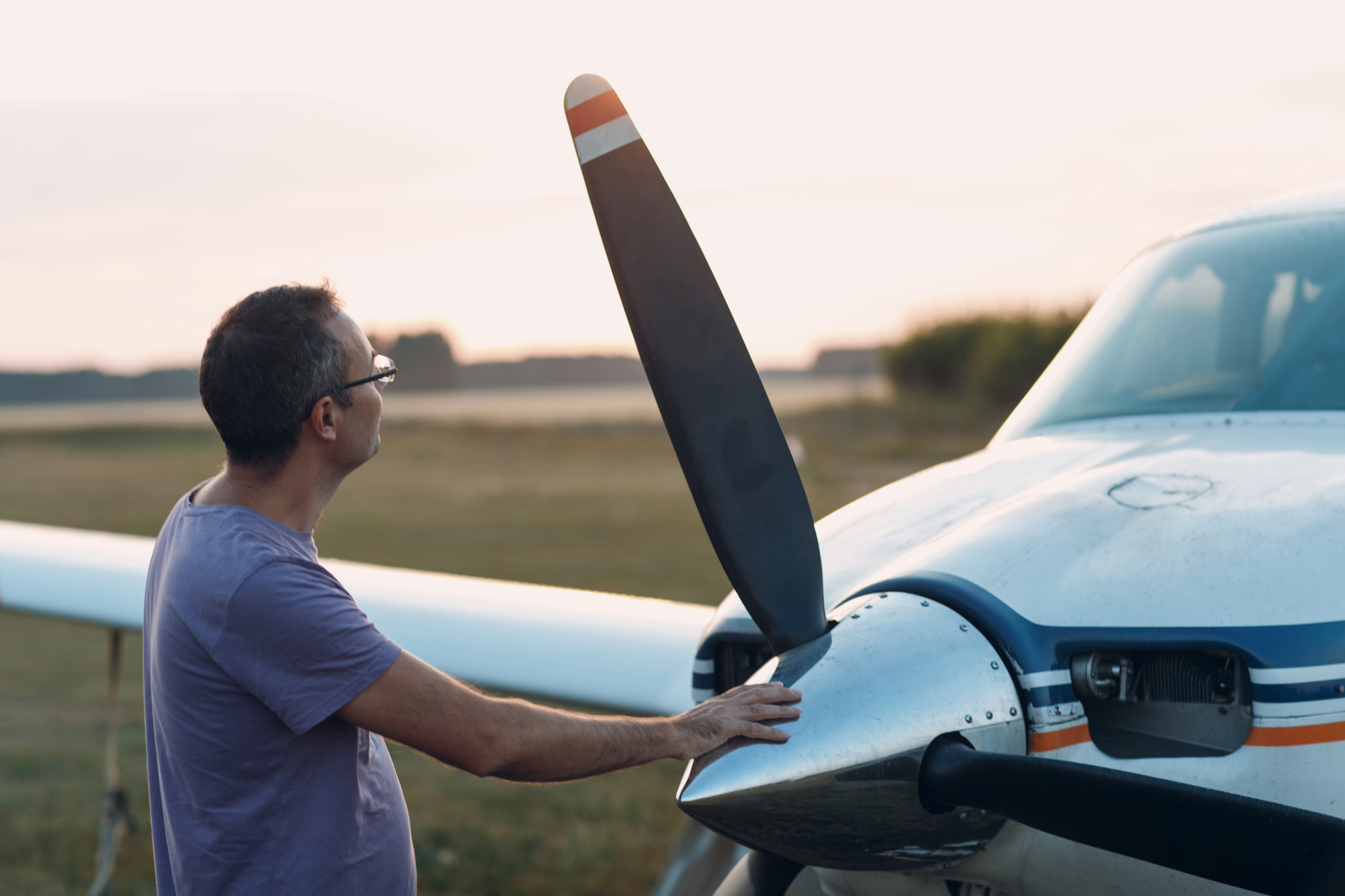 Pilot inspecting propeller near grass strip