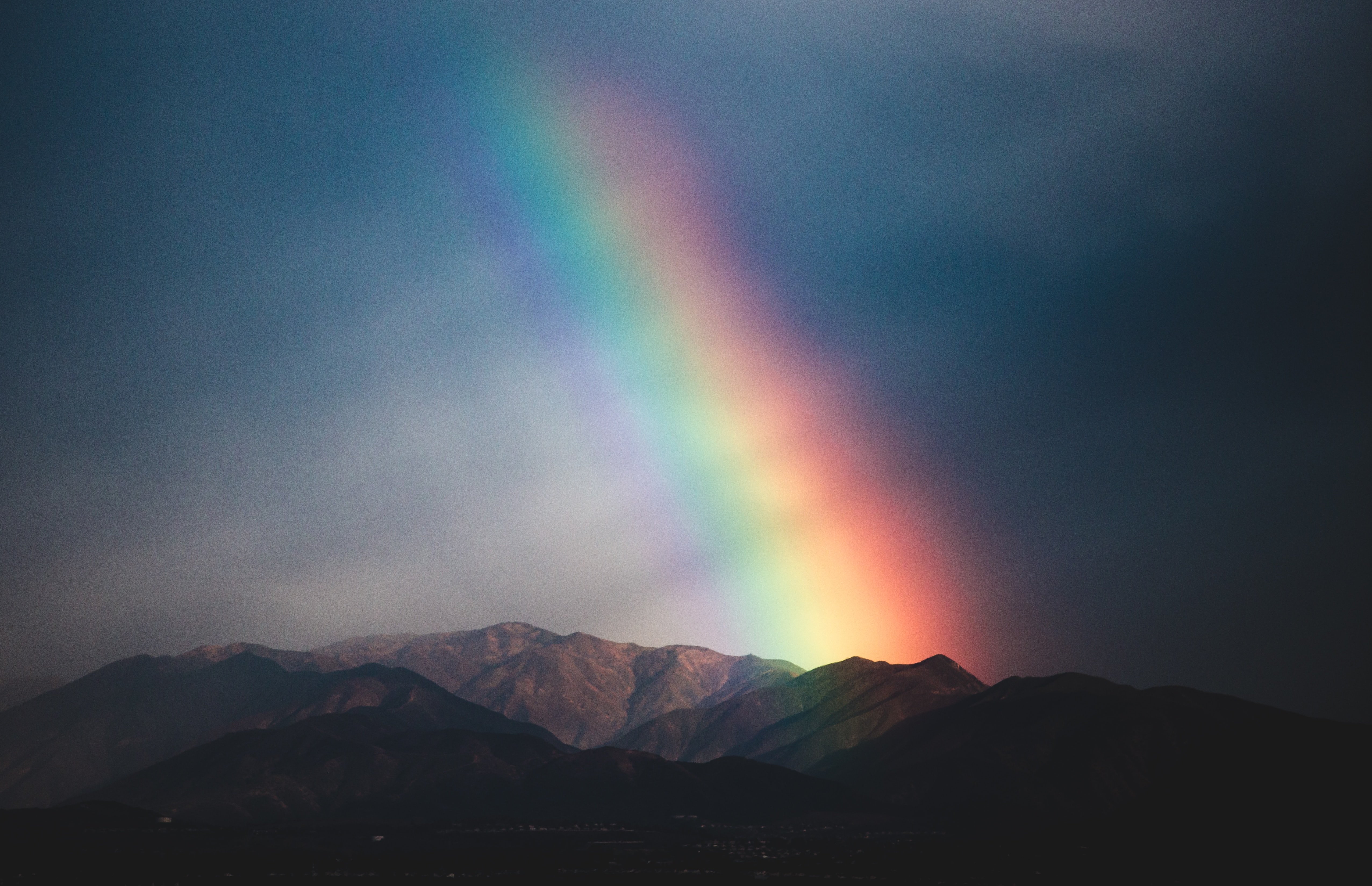 Rainbow peeking through dark clouds over the mountains